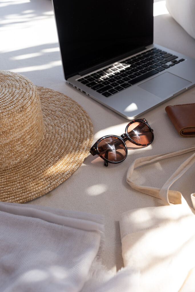 Beautiful feminine fashion summer accessories. Stylish women's sunglasses, straw hat, shopper bag, laptop in blurred sunlight shadows. Aesthetic lifestyle fashion blog, magazine, social media